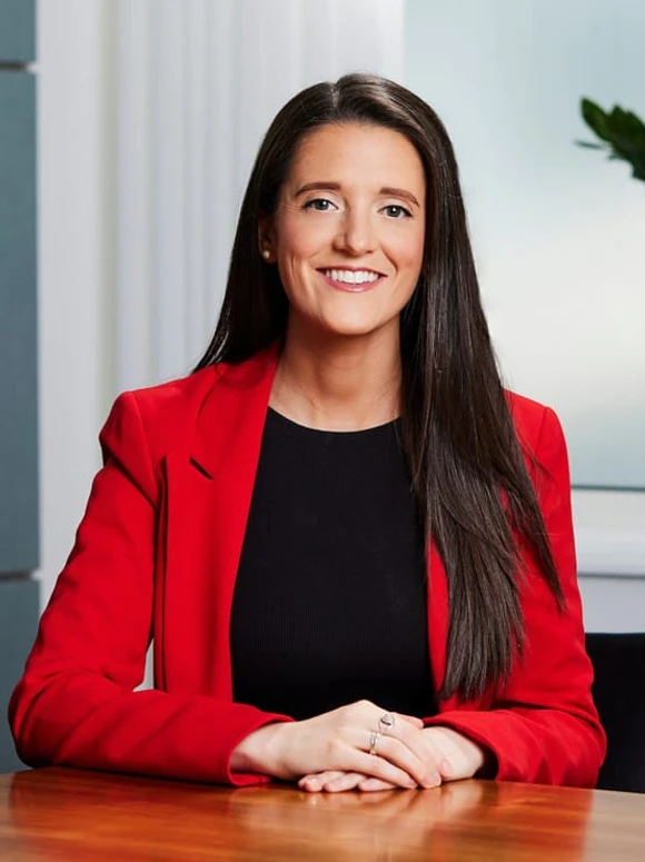 The image shows Harriet Veitch, a woman in her 30s or 40s, sitting at a desk and smiling while wearing a red jacket