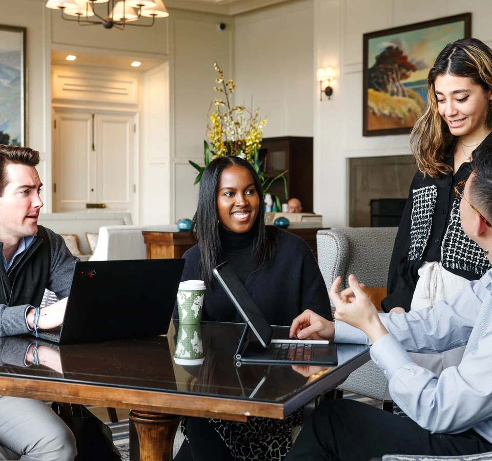 A group of young professionals having a discussion and working together with laptops in a cozy, well-appointed living room setting