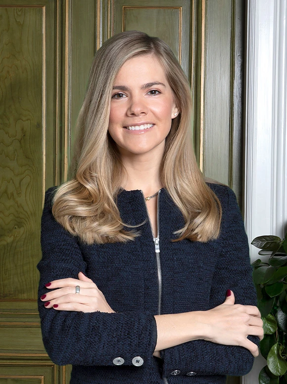 The image shows a smiling woman with long, wavy blonde hair wearing a black jacket, posing in front of a green wooden wall. The woman's name appears to be Amanda Thielemann