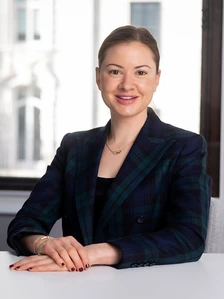 The image shows Victoria Kayser, a professional woman with short dark hair, wearing a navy and green plaid blazer, smiling at the camera in what appears to be a business setting