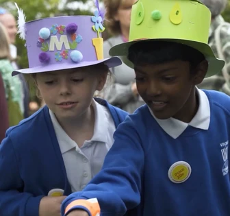 Two children wearing colorful hats and school uniforms standing together, suggesting an educational or school-related context