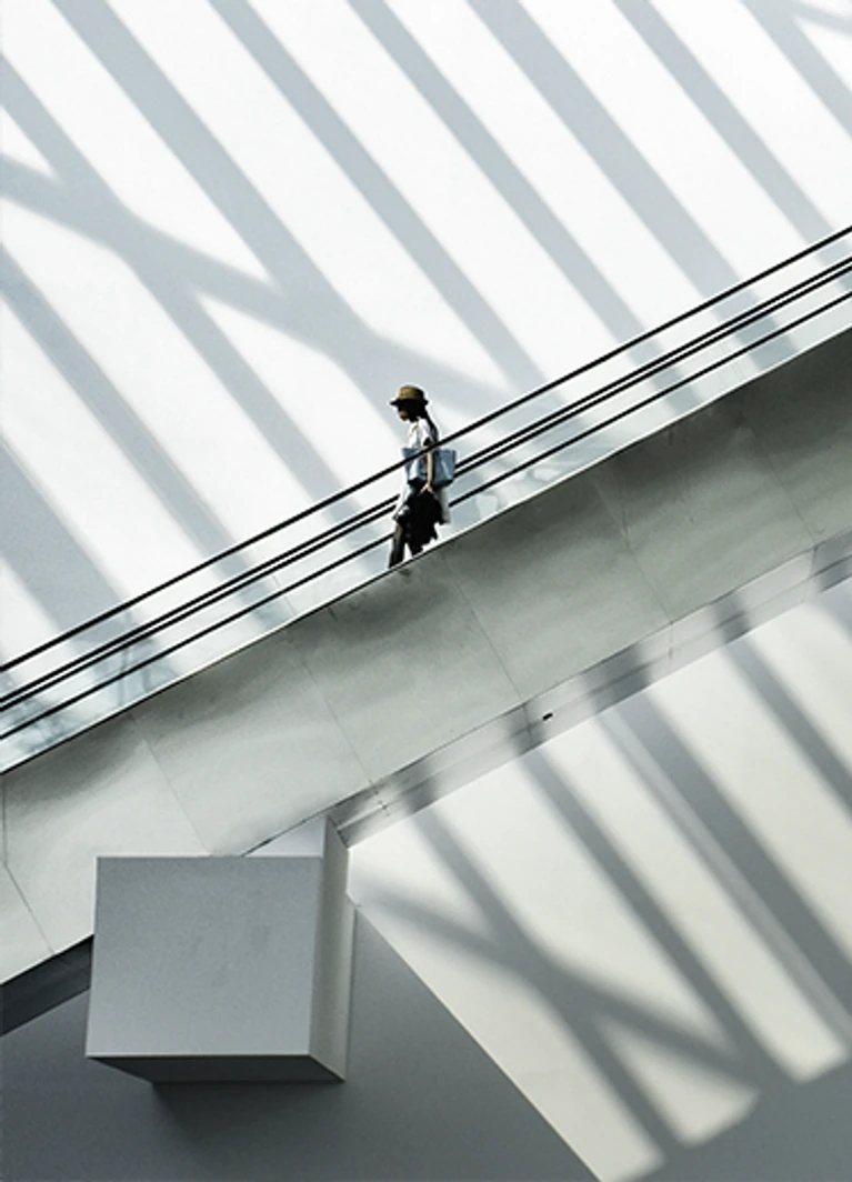 A person walking alone on a raised walkway with striking geometric architecture and dramatic lighting in the background