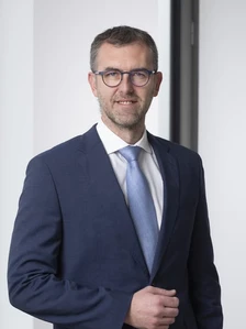 Cedric Pedoni, a businessman in a navy blue suit and tie, posing for a professional portrait with a confident expression