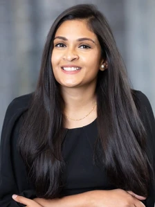 A cheerful, professional-looking woman with dark hair and a warm smile, dressed in a black blouse and posing for a portrait