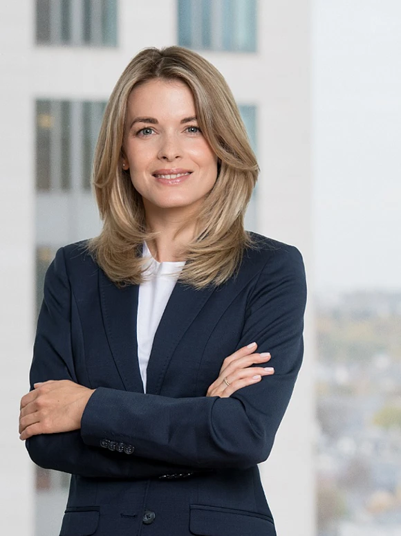 The image shows a confident-looking woman with blonde hair and blue eyes wearing a navy blue business suit, standing with her arms crossed. The filename suggests her name is Jenny Ihrig