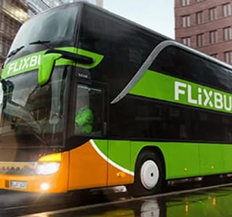 A large green and orange bus with the "FlixBus" logo, standing on a city street with tall buildings in the background