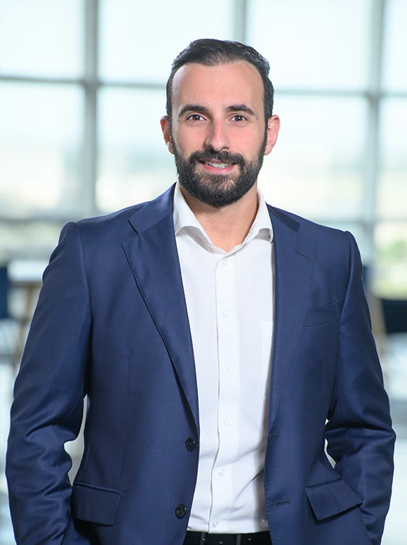 Mihail Ihaj, a bearded professional man in a navy blue suit, smiling confidently in a business setting