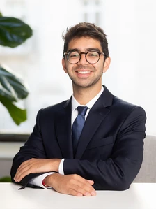 Soham Dalwani, a young professional in a suit, sits at a desk with a warm smile, conveying a confident and approachable demeanor
