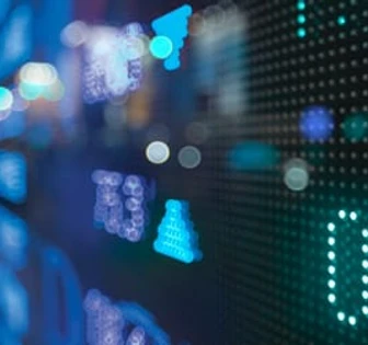 The image shows a blurred financial display with various colorful blinking lights, numbers, and patterns, suggesting a dynamic and technologically advanced financial services environment