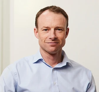 An image of Chris Pell, a middle-aged man with short brown hair, wearing a light blue collared shirt and looking directly at the camera with a friendly expression