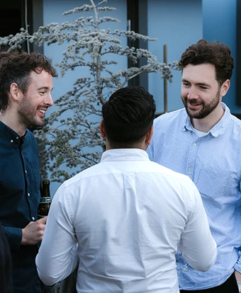 The image shows a group of five young men chatting and interacting in a snowy outdoor setting, with a decorated evergreen tree in the background