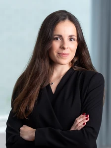 Maria Betolaza, a brunette woman with long hair, is wearing a black blouse and looking directly at the camera with a slight smile