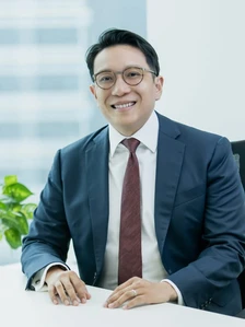 Daniel Tan, a smiling Asian man in a suit, sitting at a desk in a professional office setting