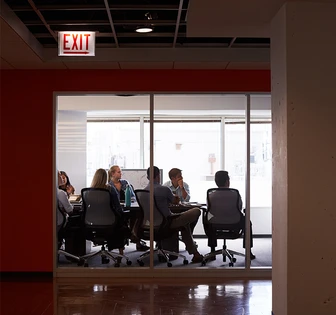 A group of professionals having a meeting in a modern office space, with an "EXIT" sign visible overhead