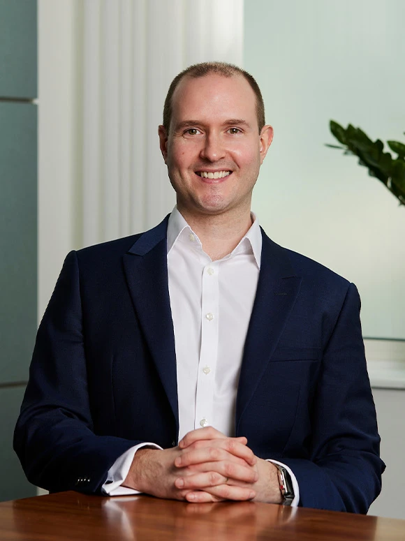 Portrait of Martyn Webb, a smiling middle-aged man in a navy blue suit, sitting at a desk