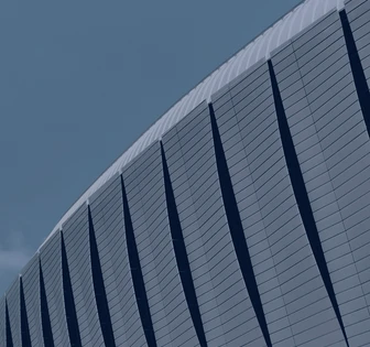 The image shows the side of a large, modern building with a curved, ribbed exterior structure against a gray sky