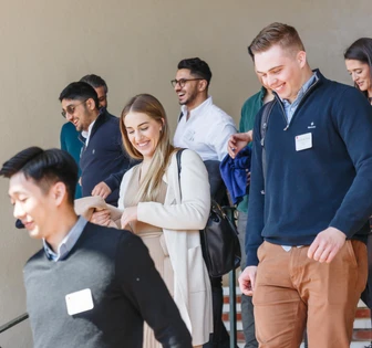 This image shows a group of casual-dressed people, including a woman with blonde hair, standing in what appears to be a meeting or conference room, suggesting a positive, collaborative work environment