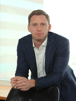 The image shows a man in a navy blue suit, sitting at a desk with a serious expression on his face. The man appears to be Chris North, based on the filename