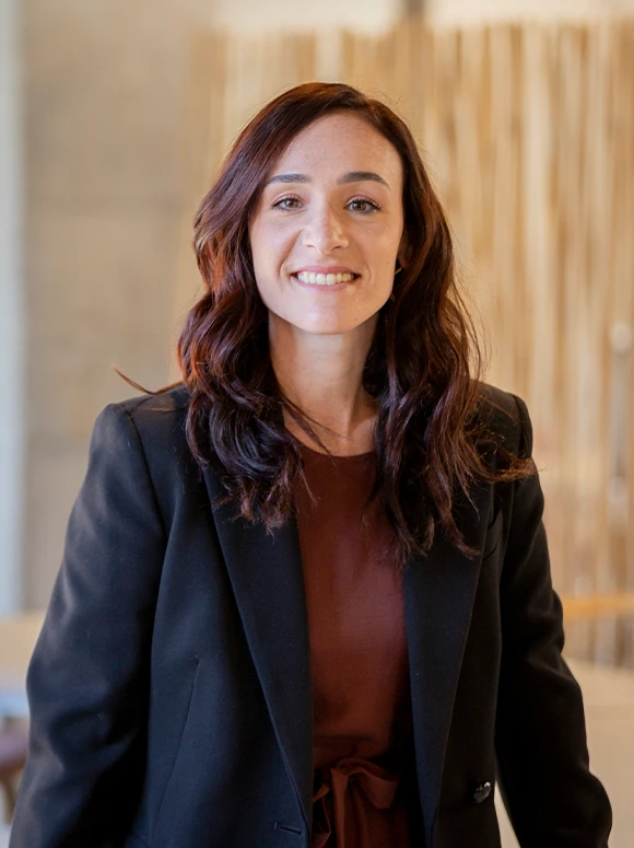 A smiling woman with long dark hair wearing a black jacket, appearing confident and professional