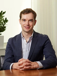 Robert Grieg, a professional businessman, sits at a desk in a modern office setting, looking directly at the camera with a friendly smile