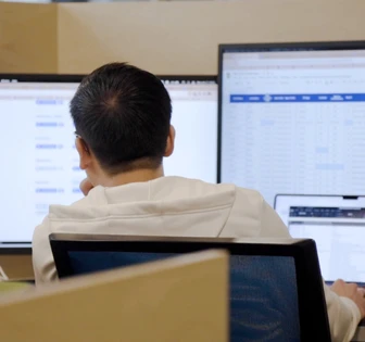 A person is sitting at a computer desk, intently focused on the screen in front of them, likely engaged in work or a task