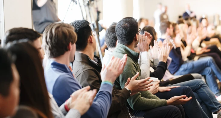 A crowd of people sitting and applauding during what appears to be a conference or event