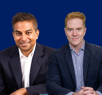 The image shows Dipan and Brian, two men sitting together wearing formal attire against a blue background