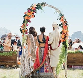 A colorful outdoor wedding ceremony with the couple standing under a floral arch, surrounded by a crowd of guests
