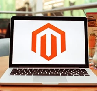 The image shows a Magento logo displayed on a laptop screen, indicating the Magento platform or e-commerce software