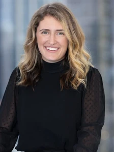 Jaclyn Daily, a woman with long, wavy blonde hair, smiling warmly at the camera in a black turtleneck sweater