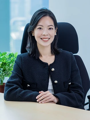 The image shows Julia Lam, a professional woman with short dark hair, wearing a black blazer, and sitting at her desk with plants in the background