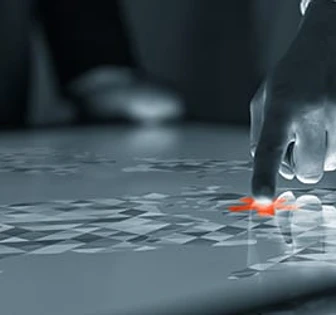 A hand reaches down to touch a lone red leaf floating on a reflective surface, creating ripples in the otherwise still, monochrome scene