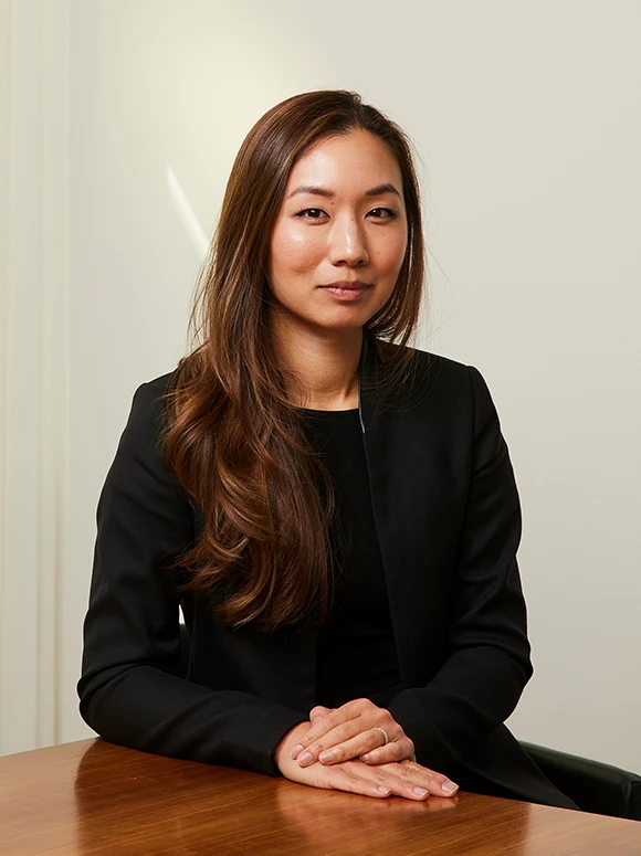 The image shows a headshot of Christine Kuo, a woman with long brown hair wearing a black jacket, posing at a desk and looking directly at the camera