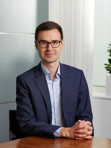 Ben Rodgers, a professional-looking man in a navy blue suit, is sitting at a desk and making eye contact with the camera