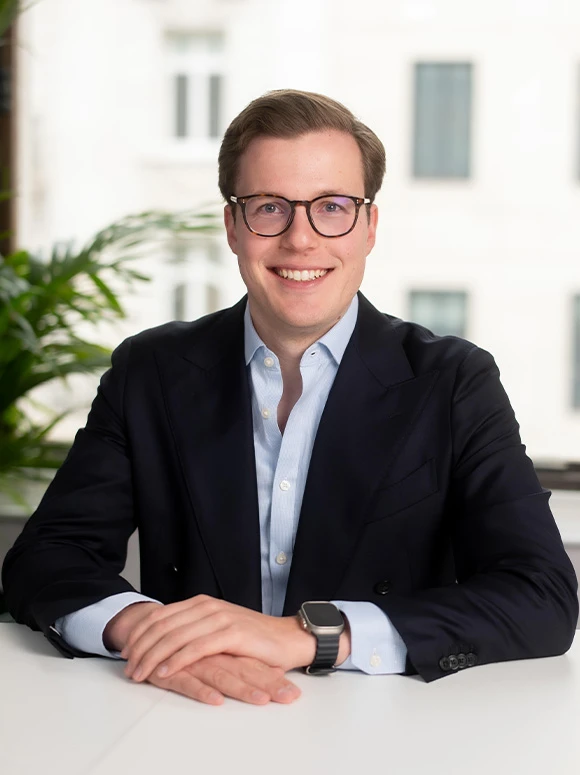 The image shows a smiling man with glasses, wearing a dark suit, sitting at a table and looking at the camera. The file name suggests his name is Ole Bick