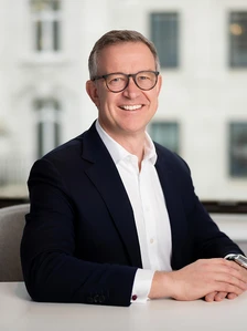Lionel Hill, a smiling man in a suit and glasses, sitting at a desk in an office environment