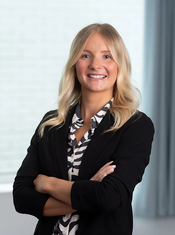 The image shows Georgia Fawkes, a smiling woman with long blonde hair, wearing a black blazer and patterned blouse, standing in front of a plain background