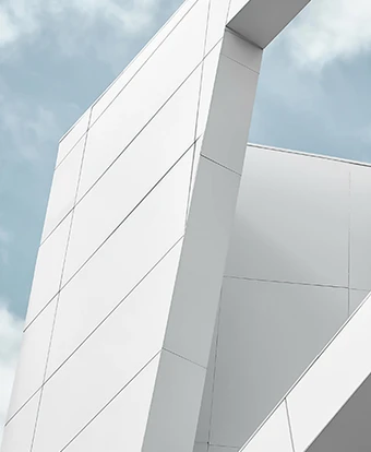 The image depicts a modern, angular building with a striking architectural design featuring intersecting white and gray panels against a cloudy sky