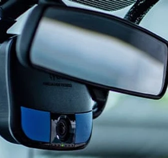 This image shows a side-view mirror of a vehicle, which appears to have a camera and sensors attached to it, likely for driver monitoring or recording purposes