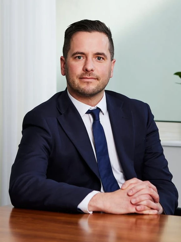 The image depicts Marcus White, a middle-aged professional businessman in a dark suit and blue tie, sitting at a desk and looking at the camera