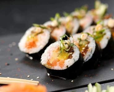 Several sushi rolls with various ingredients, arranged neatly on a dark plate with chopsticks and spices