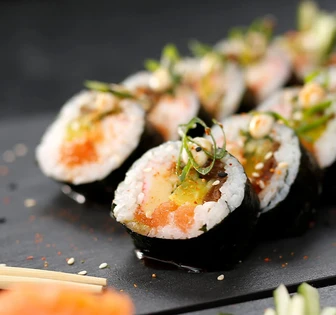 Several sushi rolls with various ingredients, arranged neatly on a dark plate with chopsticks and spices