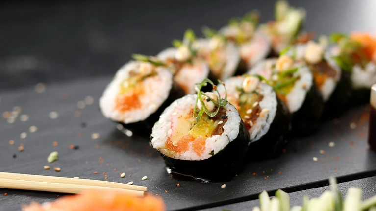 Several sushi rolls with various ingredients, arranged neatly on a dark plate with chopsticks and spices