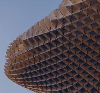 The image shows a large, spherical structure made of interlocking, triangular panels. The structure appears to be an architectural or sculptural installation, with a distinctive geometric pattern and warm, earthy tones