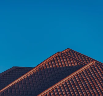 The image shows the peaked roof of a building, with rows of red tiles against a clear blue sky