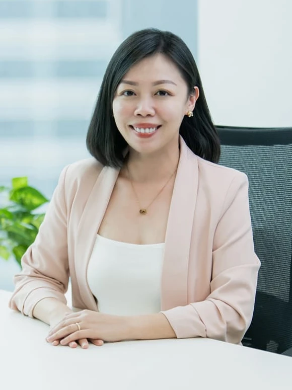 The image shows Evangeline Sim, a smiling young professional woman in a beige blazer, seated at a desk with a blurred background