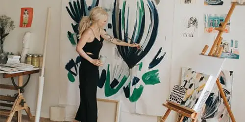 A woman painting on a large canvas. 