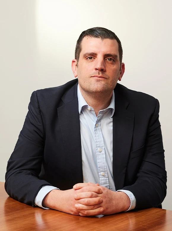 The image shows a middle-aged man in a suit, seated at a desk, with a serious expression on his face. The filename suggests this is a portrait of "Matthew Meylan"