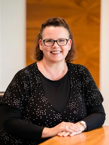 Annie Paver, a woman with short dark hair, wearing glasses and a black and white polka dot top, smiling and sitting at a desk