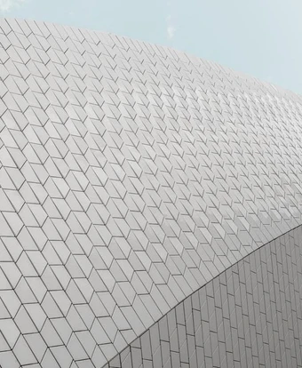 The image shows a large, modern building with a striking geometric facade composed of interlocking triangular panels, creating a visually captivating architectural design